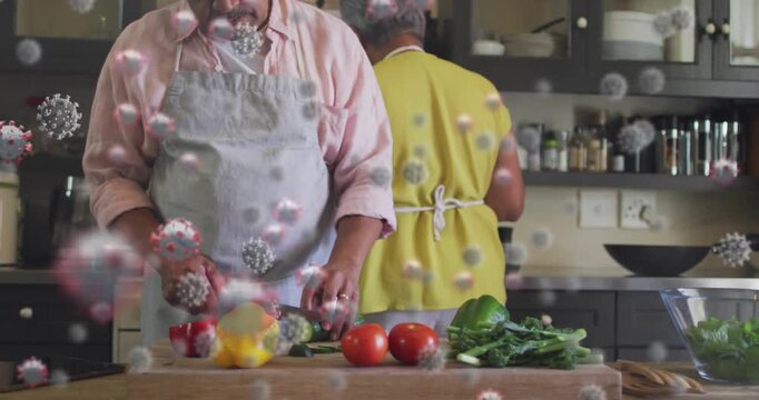 Couple placing veggies, slicing cucumber on board while viral icons obscuring frame, preparing food