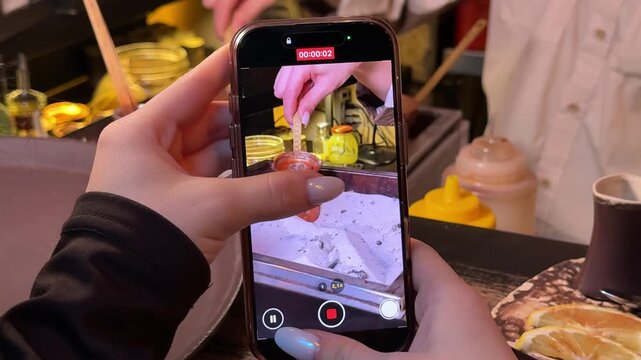A girl films coffee being made in a Turkish coffee pot on the sand on her mobile phone. Blog Professional barista carefully weighing and pouring hot water from copper kettle onto freshly ground