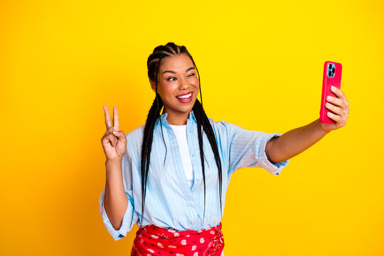 Young woman taking a selfie with peace sign against bright yellow background