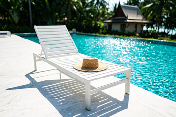 Obraz premium Straw Hat on White Lounger by Luxury Swimming Pool at Tropical Resort