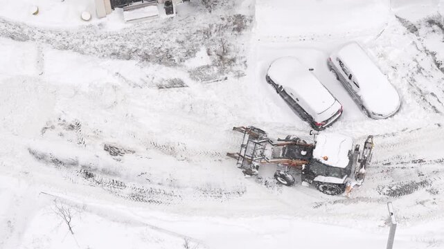 Aerial drone view of snow removal machinery clearing road in winter industrial area, heavy equipment working in harsh weather conditions