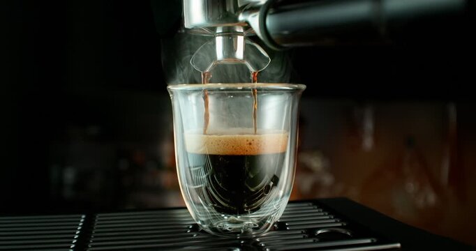 Super slow motion close-up of espresso pouring from a coffee machine into a glass cup. Rich crema forms on the surface as dark coffee flows, highlighting texture, aroma and detail of fresh coffee prep