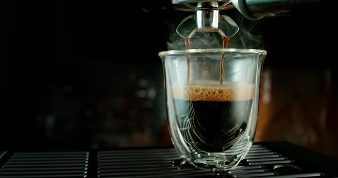 Super slow motion close-up of espresso pouring from a coffee machine into a glass cup. Rich crema forms on the surface as dark coffee flows, highlighting texture, aroma and detail of fresh coffee prep