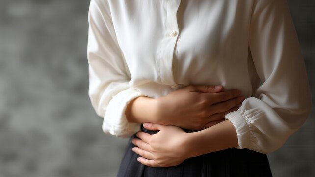 お腹を押さえる女性の手元。腹痛や体調不良のイメージ素材。
