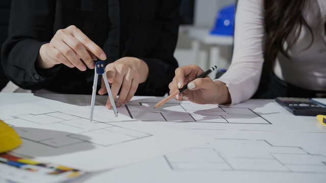 Two architects drafting building floor plans on a table using compass and pencil, close-up of hands and architectural drawings