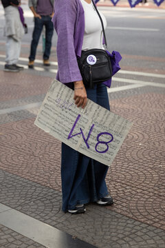 Mujer en la marcha de la mujer sosteniendo un cartel con partituras musicales y el 8m escrito en el. Mujer vestida de violeta en la marcha por los derechos de las mujeres. 