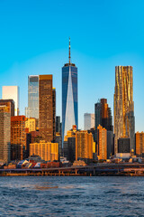 Fototapeta premium Modern office towers and residential buildings of downtown Manhattan, New York are reflected in the moving waters of the East River during a clear morning as seen from Brooklyn.