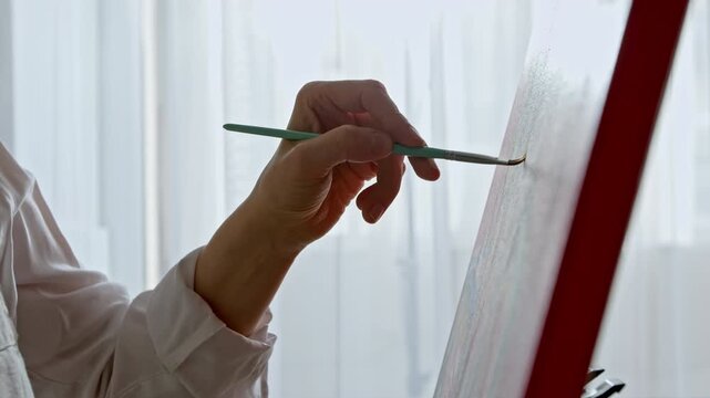 Artist hand painting expressive male portrait on canvas with brush and palette.