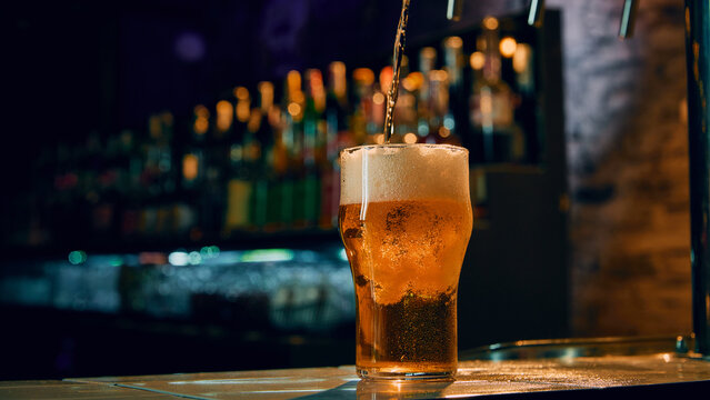 Fresh beer being poured into glass at bar counter with foam forming on top. Concept of beverage service promotion, bar menu visual, drink advertising, hospitality marketing, product presentation.