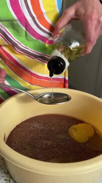 Vertical side view video: oil is gradually added with a large spoon into a bowl with liver and eggs, cooking process