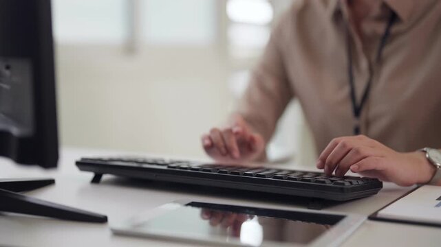 Focused adult Asian business professional typing computer keyboard completing tasks modern office workspace