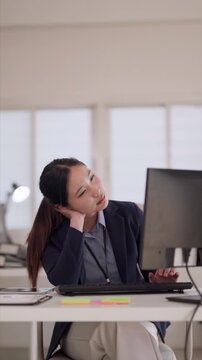 Asian adult businesswoman experiences neck pain stress fatigue overworked at desk modern office computer use ergonomic issues