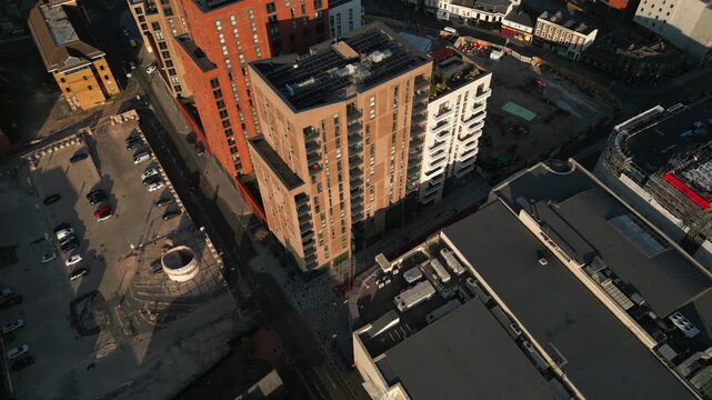 An aerial view showcases urban development with modern apartment buildings, a construction site, and a parking lot filled with cars.