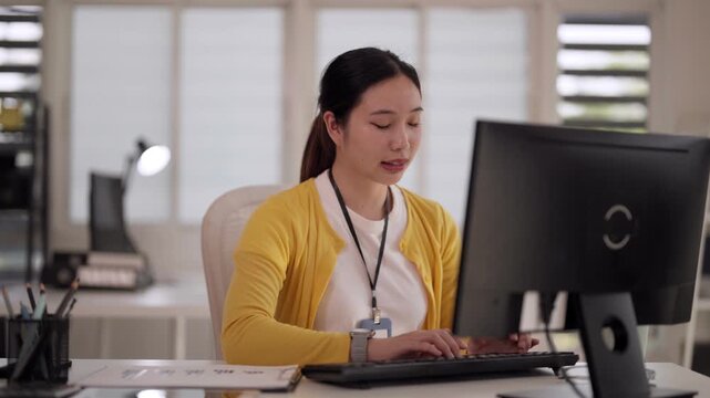 Asian adult woman professional focused typing keyboard desktop computer office workplace employee productive online business research education environment