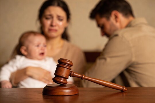 Martillo de juez en primer plano con una madre llorando, un beb&eacute; y un padre desenfocados en el fondo. Concepto de divorcio, separaci&oacute;n y custodia legal infantil