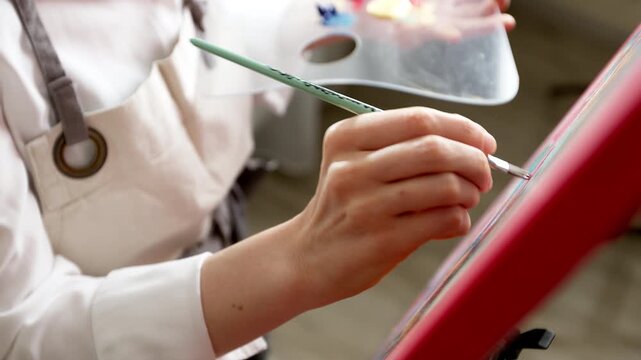 Close up of artist hand painting male portrait with brush and palette.