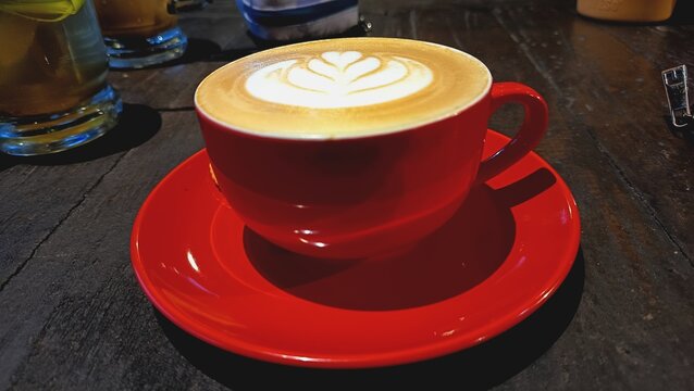 Top view of creamy latte art coffee in red cup on wooden table. Beautiful heart-shaped foam design creates warm and cozy cafe atmosphere, perfect for food, beverage, and lifestyle concept