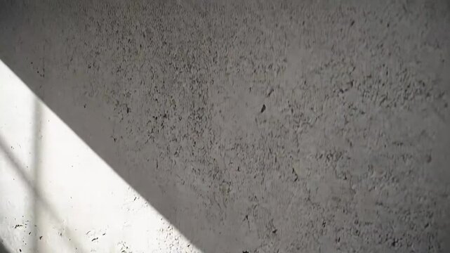 Rough concrete wall featuring an uneven textured surface and contrasting patterns of light and shadow, creating a minimalist architectural background with abstract visual interest