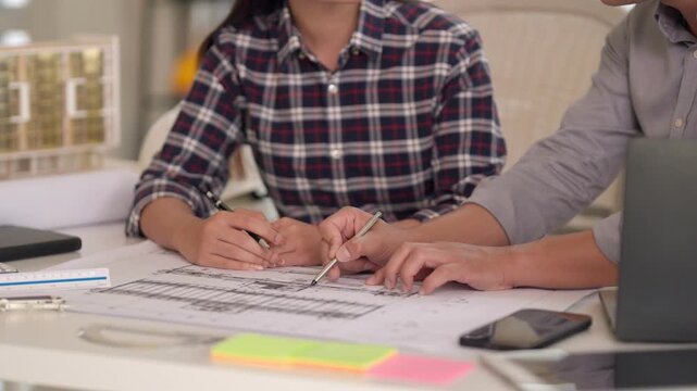 Asian adult architects engineers collaborating discussing architectural building project blueprints detailed design plans professional office teamwork urban development innovation strategy