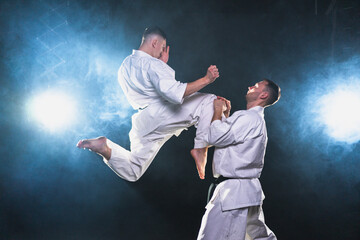 Martial arts masters on dark background. Strong man fighters in white kimono for karate martial arts fighting training in black gym. Karate fighters training punches kicks practicing fight sparring © Юлия Завалишина