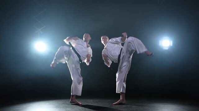 Martial arts masters on dark background. Strong man fighters in white kimono for karate martial arts fighting training in black gym. Karate fighters training punches kicks practicing fight sparring