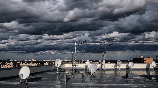 Stormy roof with satellite dishes and antennas, dark rolling clouds filling sky above wet reflective rooftop, multiple parabolic dishes and masts, urban skyline and low buildings on horizon, dramatic