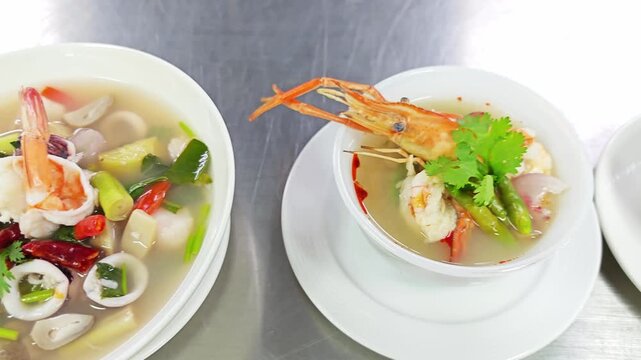 Authentic Thai cuisine: Clear Tom Yum soup with shrimp, lemongrass, and galangal in a white bowl.