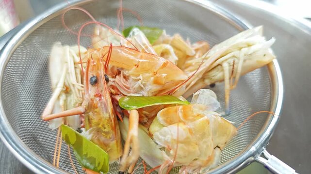 Boiled river shrimp heads with kaffir lime leaves in a metal strainer for making Tom Yum soup.