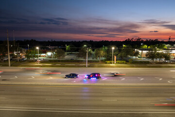 Nighttime traffic stop on USA city street as police pull over speeding vehicle. Patrol car lights flash in urban traffic environment. © bilanol