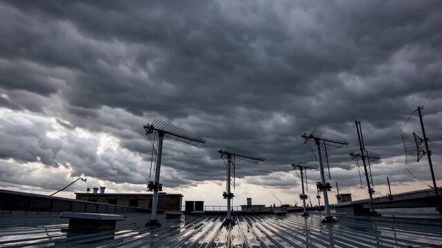 stormy construction site rooftop with cranes dark heavy clouds sweeping over steel beams, wet corrugated roof reflecting distant skyline, row of tower cranes silhouetted against low sun glow, tense