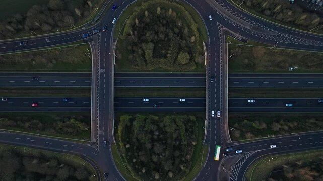 Cinematic aerial drone footage of a modern highway interchange on the N4 road in Ireland during evening golden hour. Smooth traffic flow with cars moving through curved roads surrounded by lush green.
