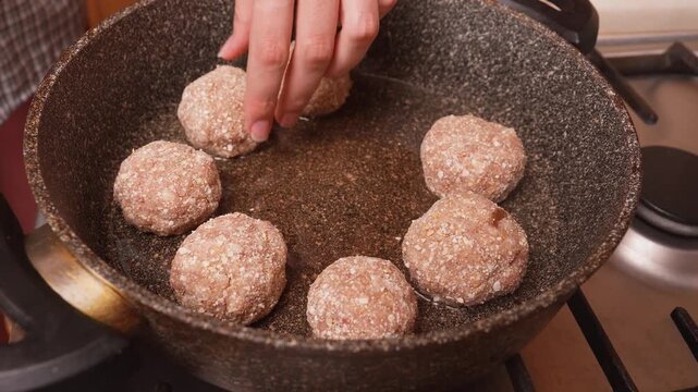 Pan with raw meatballs or catlets, home cook lays out seasoned meatballs in a hot pan to sear the edges of the gas stove, hands nearby set the distance for even searing and subsequent sauce