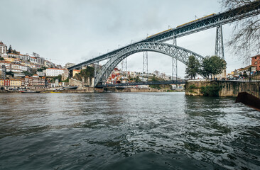 Obraz premium The Dom Luís I Bridge spanning across the Douro River in Porto, Portugal, showcasing its iconic double-deck metal arch architecture against a historic city backdrop for travel and tourism concepts