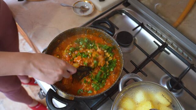 simmering stew topped with fresh parsley as hands stir pot, vibrant green scattered over thick tomato base, steaming pan beside boiled potatoes, finishing touch for family meal