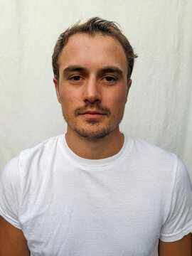 A portrait of a tanned young man wearing a white shirt with a white background and looking at the camera.