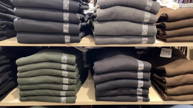 Stacked sweaters on shelves in a clothing store, showcasing various colors and sizes