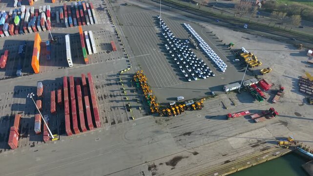 Aerial video of the Seaforth terminal at the Port of Liverpool, showing rows of imported vehicles, heavy construction machinery, and shipping containers under the morning sun in England.