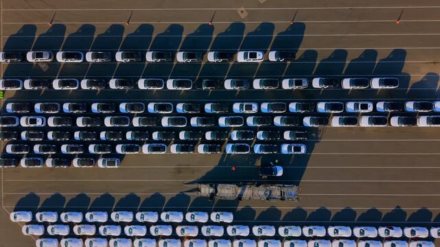 Aerial video of rows of new vehicles parked at terminal, Port in UK, showing long morning shadows and precise organization in automotive logistics.