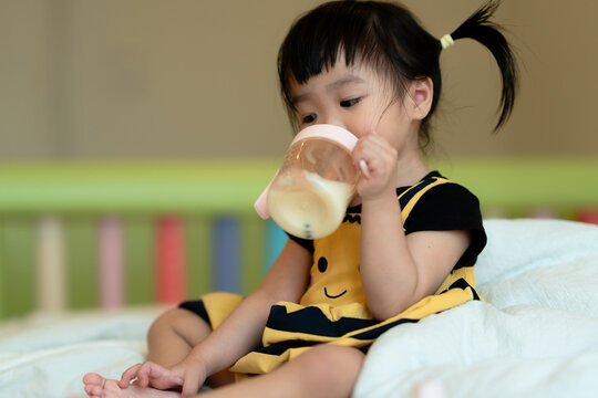 A toddler wearing a yellow outfit is hungrily drinking milk in the room.