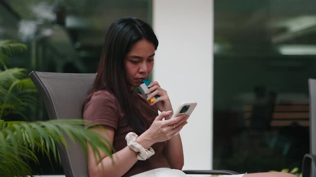 Young woman vaping an electronic cigarette and using a smartphone outdoors