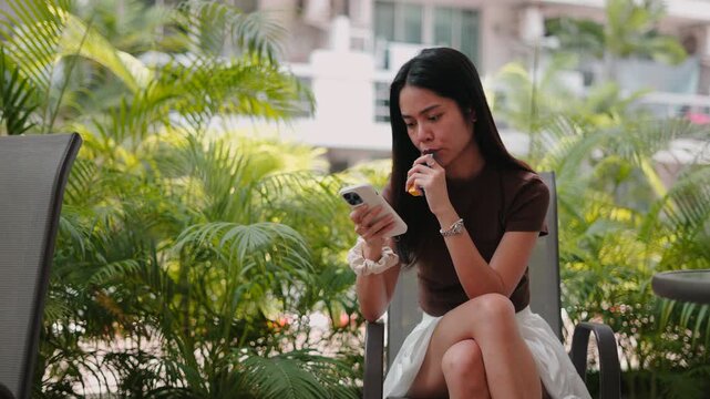 Woman vaping an e cigarette and using smartphone sitting on a modern balcony