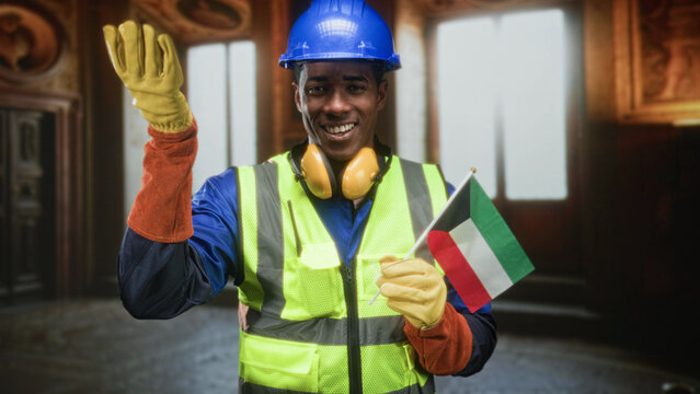Man construction worker holding kuwaiti flag and raising gloved hand in building interior; pride unity celebration.