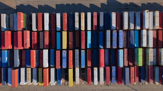 Vertical aerial video looking down on rows of colorful shipping containers at the UK Port terminal, creating a rhythmic industrial pattern with long morning shadows. 