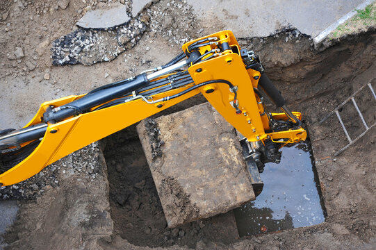 Excavator lifts slab on flooded underground water pipe