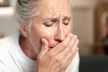 Elderly woman feeling unwell and coughing, covering her mouth