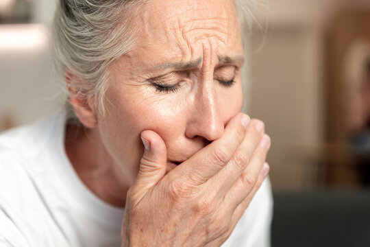 Elderly woman feeling unwell and coughing, covering her mouth
