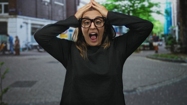 Woman with hand on forehead in a surprised gesture on a busy street wearing dark glasses and casual sweater, facing camera; surprise reaction.