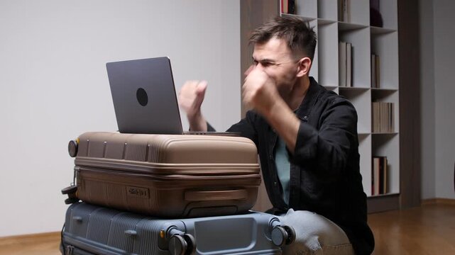 Stressed man slumped on stacked luggage, working on a laptop while facing travel delays and remote work challenges, exhausted and anxious as he waits for a canceled trip to resume