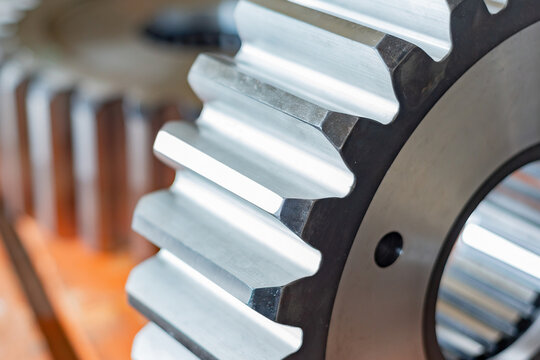 Close-up view of metallic gear in a workshop with focus on teeth and shaft during manufacturing process