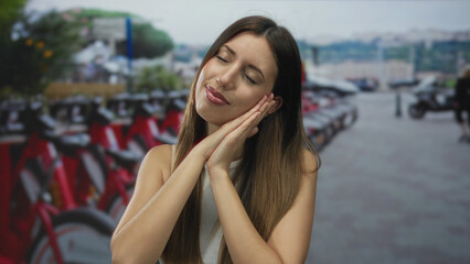 Fototapeta premium Young hispanic woman rests head on hands beside bike rack on street during bike rental; restful calm.